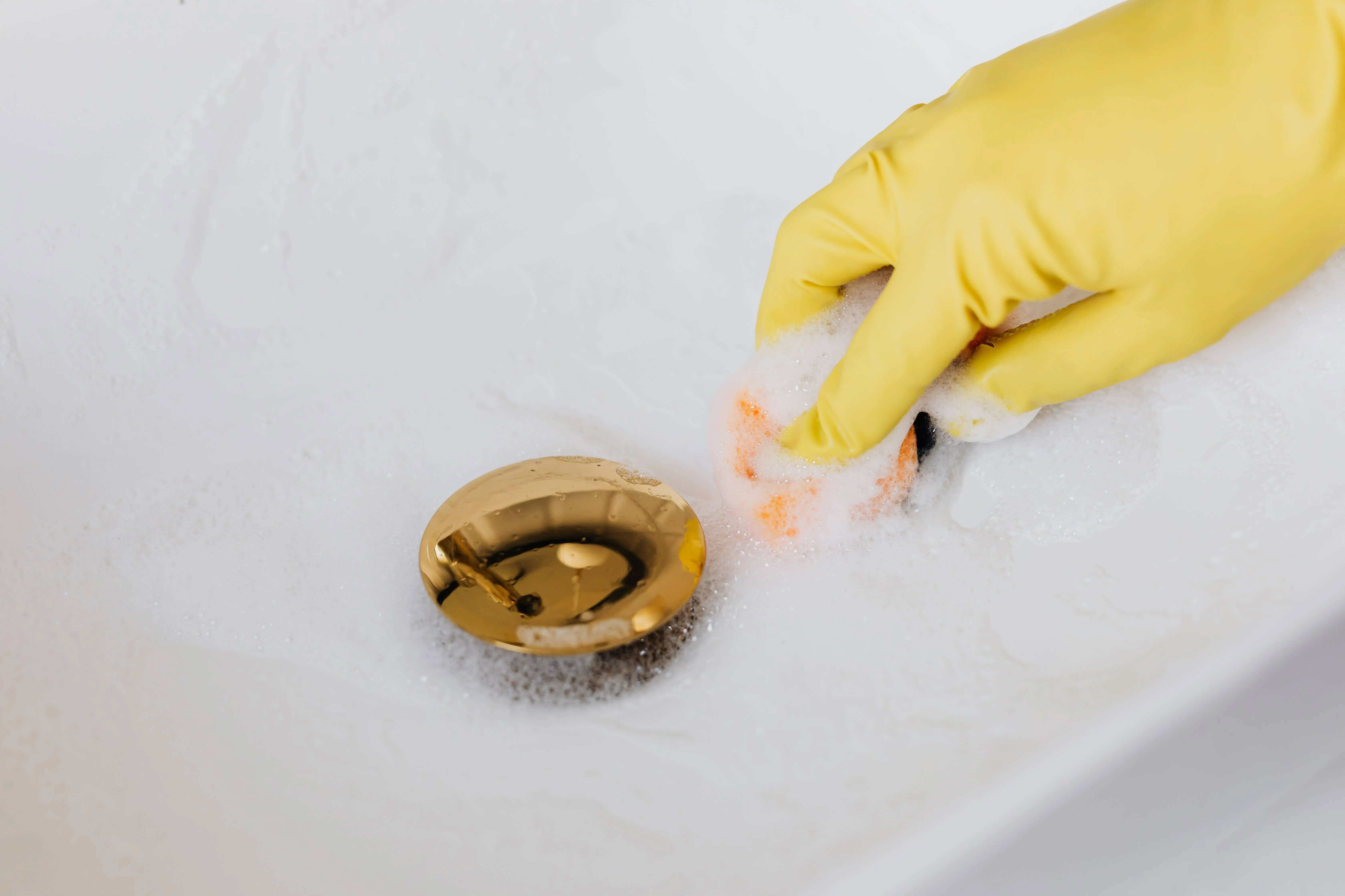 Hand in a glove holding a sponge cleaning a drain